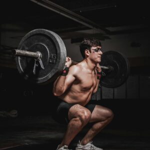 Shirtless man performing a barbell squat, showcasing strength and fitness.